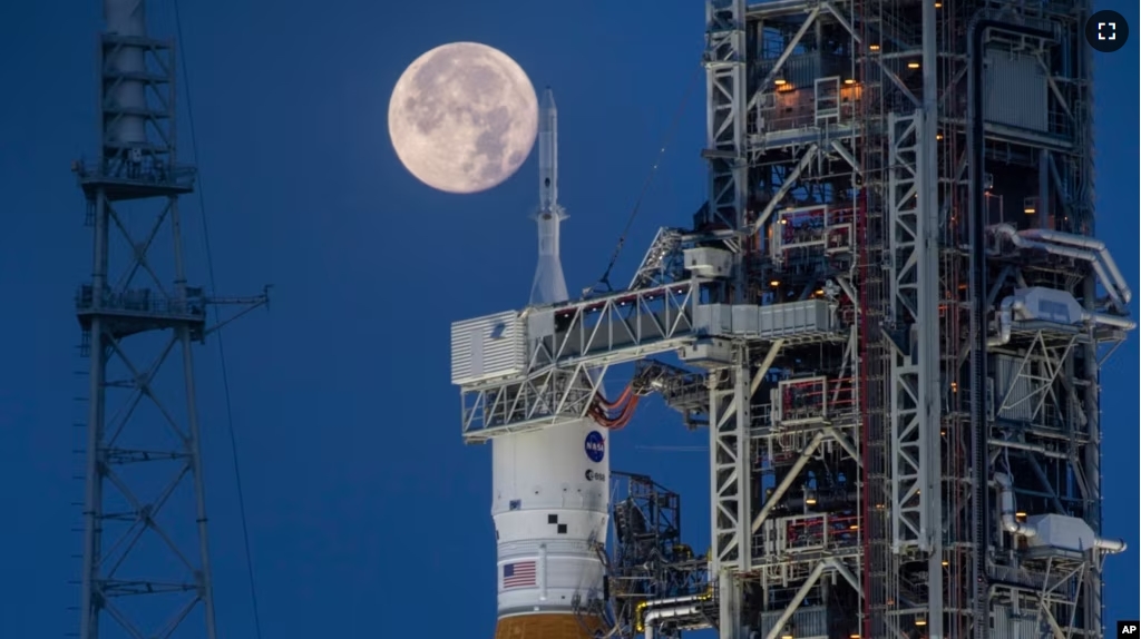 A full moon is seen behind the Artemis I Space Launch System (SLS) and Orion spacecraft, atop the mobile launcher, at NASA's Kennedy Space Center in Florida on June 14, 2022. (Cory Huston/NASA via AP)