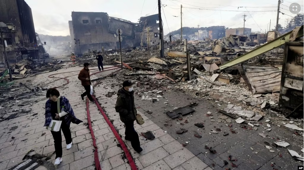 People walk past collapsed buildings following an earthquake in Wajima, Ishikawa prefecture, Japan Tuesday, Jan. 2, 2024. (Kyodo News via AP)