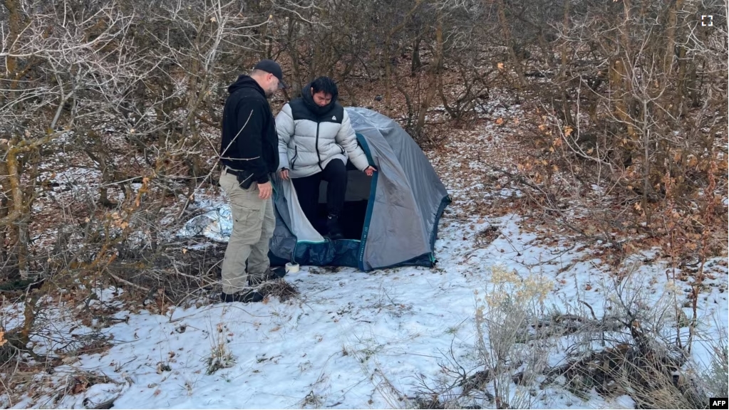 This handout photo released by the Riverdale Police Department on January 1, 2024 shows a police officer standing next with Kai Zhuang in the mountains near Brigham City, Utah, on December 31, 2023, after being reported missing. (Photo by Riverdale Police Department / AFP)