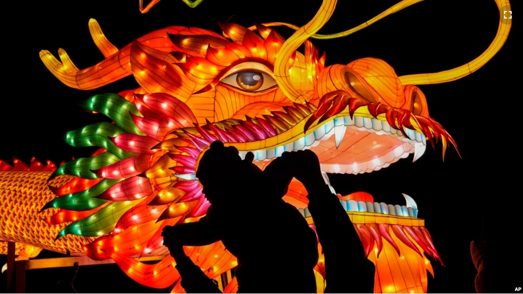 A man holds a child in front of a giant dragon lantern decoration near the popular Houhai Lake in Beijing, China on February 8, 2024. (AP Photo/Andy Wong)