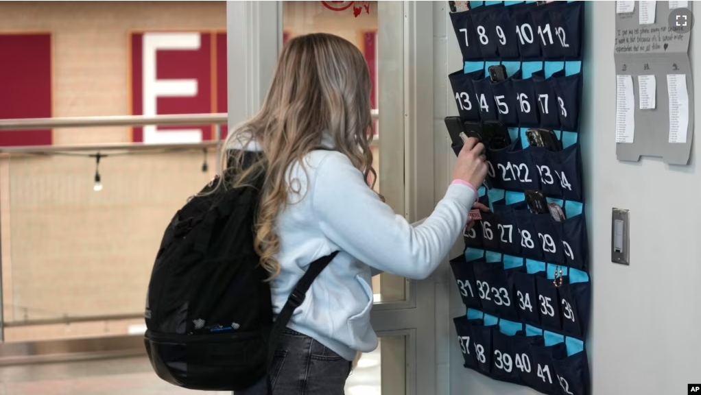 A ninth grader places her cellphone into a phone holder as she enters class at Delta High School, Friday, Feb. 23, 2024, in Delta, Utah. (AP Photo/Rick Bowmer)