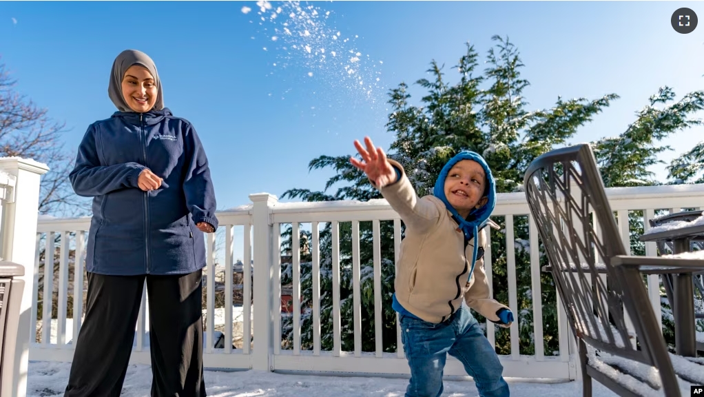 Omar Abu Kuwaik throws snow shortly after arriving from Gaza at the residence of the Global Medical Relief Fund as Khaolah Obahi of Rahma Worldwide looks on, Wednesday, Jan. 17, 2024. (AP Photo/Peter K. Afriyie)