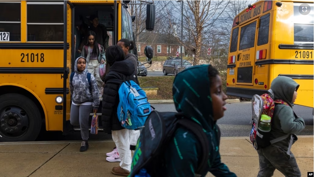 Rock Creek Forest Elementary School students exit a diesel bus before attending school, Friday, Feb. 2, 2024, in Chevy Chase, Md. At right is an electric school bus. (AP Photo/Tom Brenner)