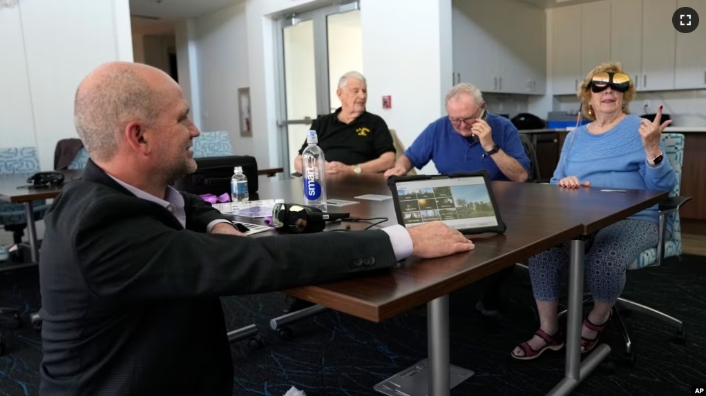 Tracy Hall, vice president of sales at Mynd Immersive, left, watches as Karen Audet, 82, right, reacts while wearing a virtual reality headset at John Knox Village, Wednesday, Jan. 31, 2024, in Pompano Beach, Fla. (AP Photo/Lynne Sladky)