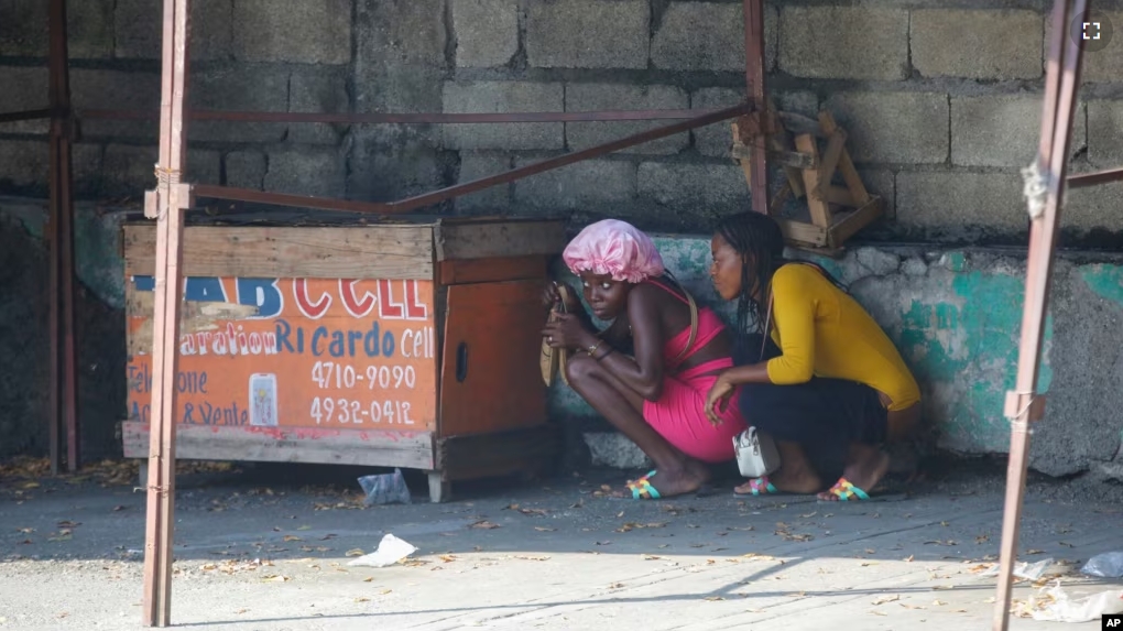 FILE - Women take cover during a gun battle between police and gang members in Port-au-Prince, Haiti, Friday, March 1, 2024. (AP Photo/Odelyn Joseph)