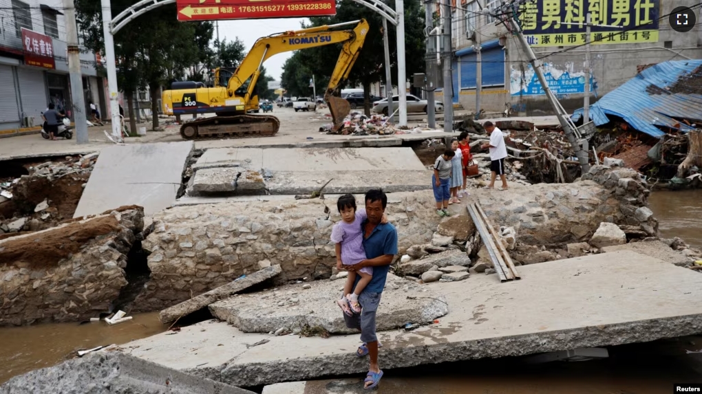 FILE - A man holding a child walks across a damaged bridge after rains and floods brought by remnants of Typhoon Doksuri, in Zhuozhou, Hebei province, China August 7, 2023. (REUTERS/Tingshu Wang)