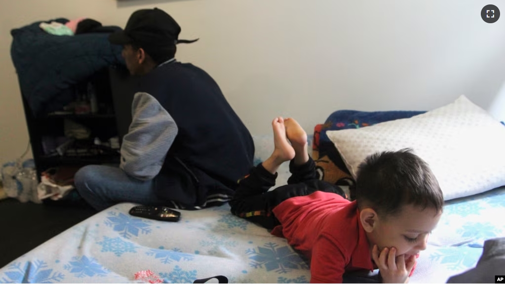 Four-year-old Fraiber Peraza looks at a phone while Franklin Peraza sits on an inflatable bed in their 'micro apartment' in Seattle on Monday, March 11, 2024. (AP Photo/Manuel Valdes)