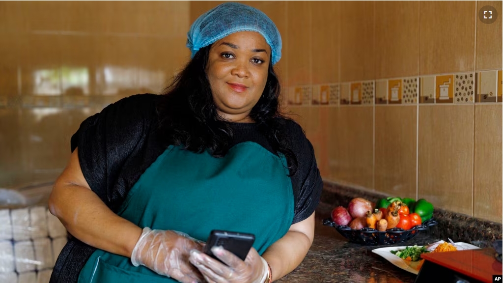 Anita Akpeere, who uses her mobile phone to run her business, stands inside her restaurant in Accra, Ghana, Tuesday, April 23, 2024. (AP Photo/ Misper Apawu)