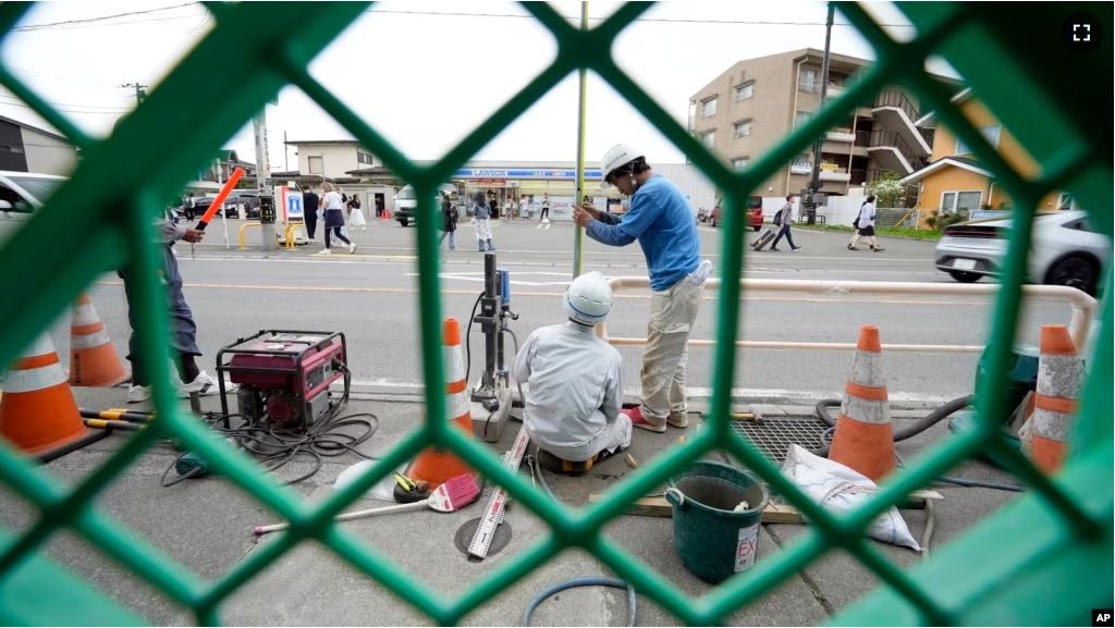 Workers set up a barricade near the Lawson convenience store, background, Tuesday, April 30, 2024, at Fujikawaguchiko town, central Japan. (AP Photo/Eugene Hoshiko)