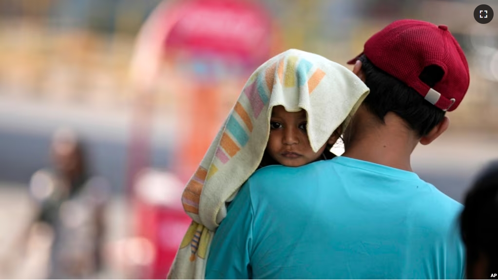 A man carries a child with its head covered with a towel to protect it from the heat in Jammu, India, Sunday, June 2, 2024. (AP Photo/Channi Anand)