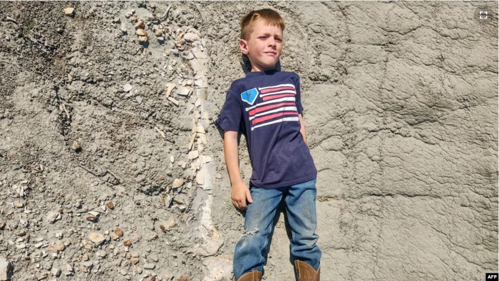 This undated handout picture provided by Giant Screen Films shows Liam Fisher lying next to his discovery - the femur and tibia of a juvenile T. rex in Marmarth, North Dakota. (Photo by Handout / Giant Screen Films / AFP)