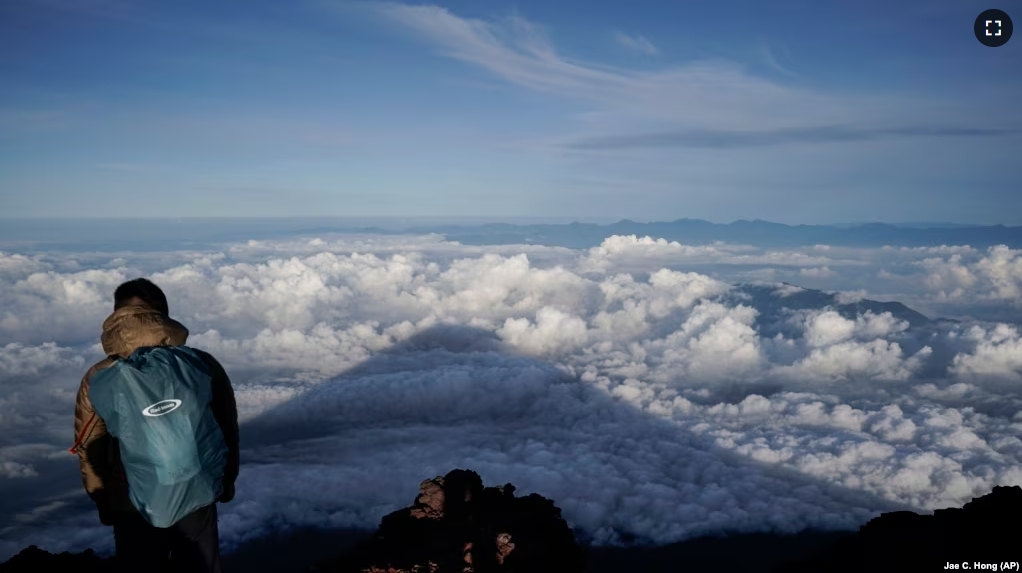 FILE - The shadow of Mount Fuji is cast on clouds hanging below the summit, Tuesday, Aug. 27, 2019, in Japan. Those who want to climb the mountain will now have to reserve ahead and pay a fee. (AP Photo/Jae C. Hong, File)