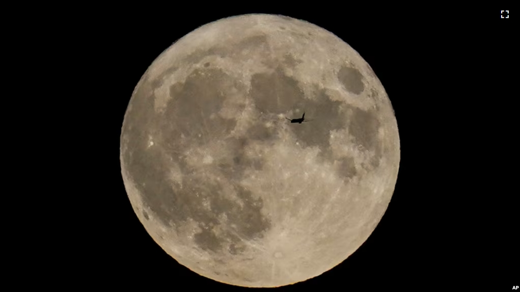 FILE - A plane passes in front of the moon, Aug. 30, 2023, in Chicago. Scientists have confirmed a cave on the moon and suspect there are hundreds more that could house future astronauts. (AP Photo/Kiichiro Sato, file)