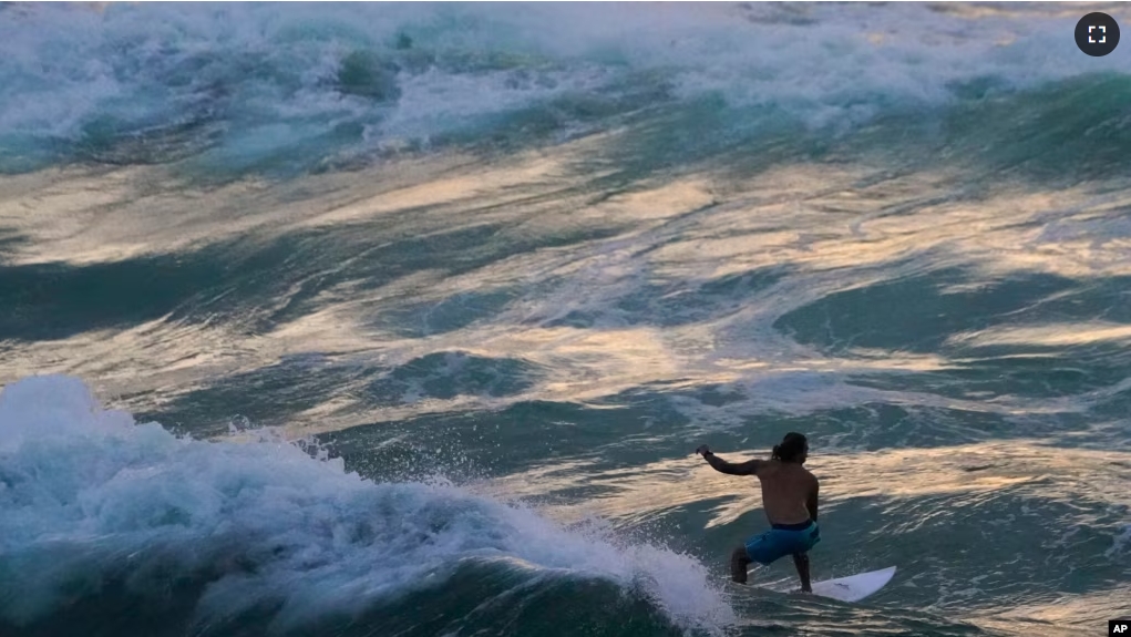 FILE - A surfer rides a wave as the color of the sky is reflected on the water in Navarre Beach, Fla., Monday, June 17, 2024. (AP Photo/Kiichiro Sato)