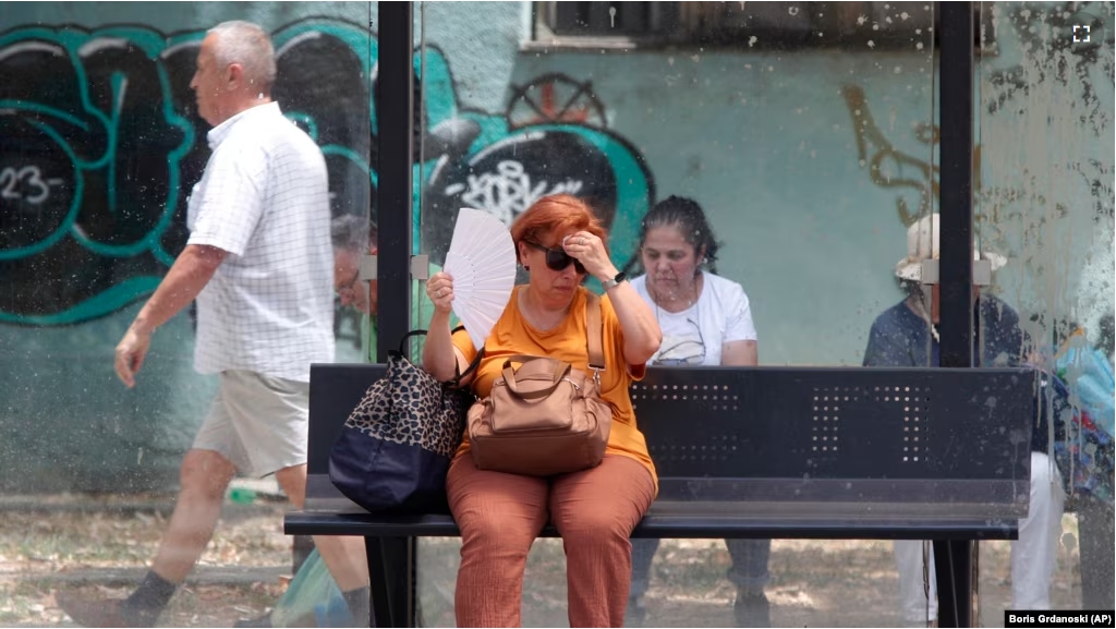 FILE - A woman tries to cool herself while waiting for a bus on a hot day in Skopje, North Macedonia, June 20, 2024. (AP Photo/Boris Grdanoski)