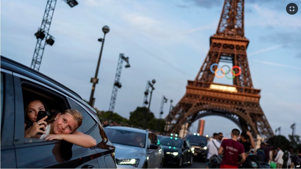 Passengers in the back of a taxi film themselves as they leave the Eiffel Tower decorated with the Olympic rings ahead of the 2024 Summer Olympics, Wednesday, July 17, 2024, in Paris. (AP Photo/David Goldman, File)