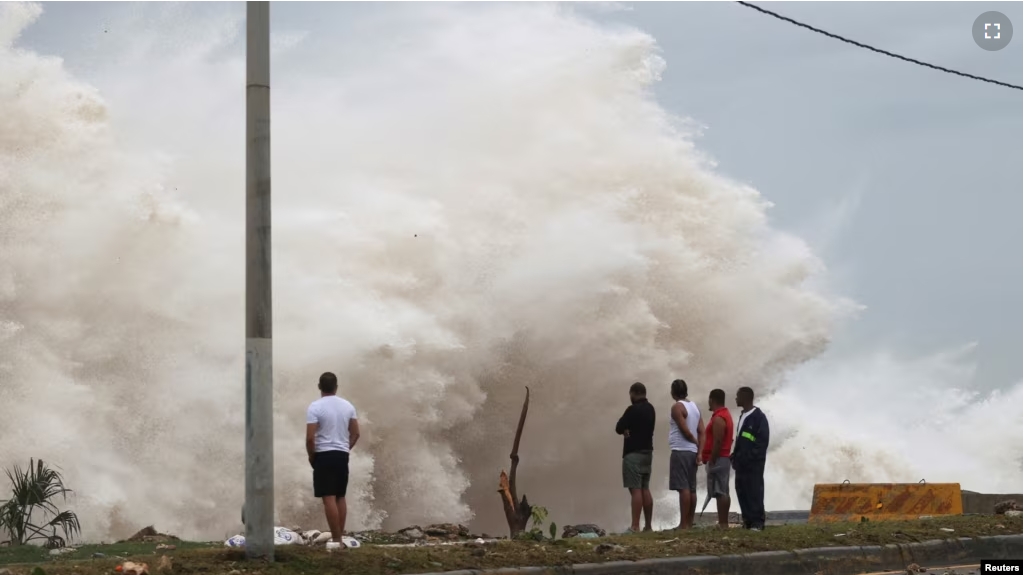 People stand in front of waves crashing against the shore as Hurricane Beryl moves south of the island, in Santo Domingo, Dominican Republic July 2, 2024. (REUTERS/Erika Santelices)