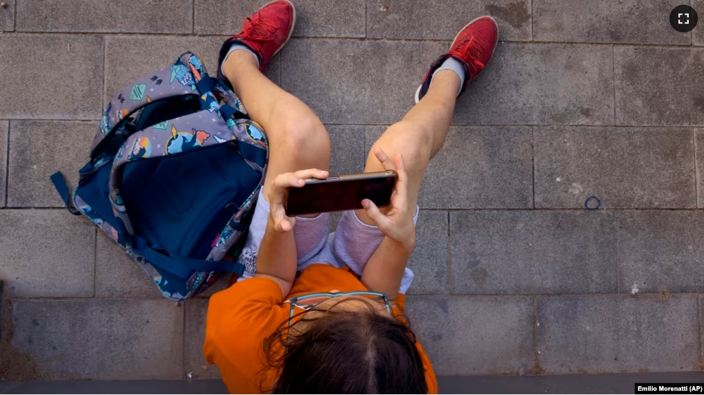 FILE - A boy plays with his father's phone outside school in Barcelona, Spain, on June 17, 2024. (AP Photo/Emilio Morenatti)