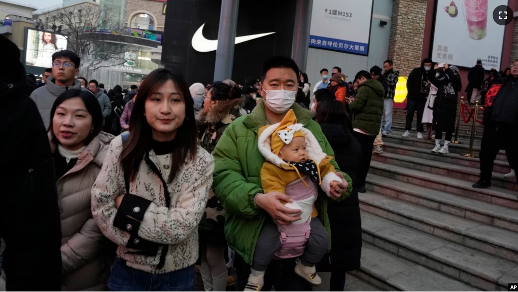 FILE - A man carries a child at a shopping mall in Beijing, Dec. 30, 2023. China’s population dropped by 2 million people in 2023 in the second straight annual drop as births fell and deaths jumped. (AP Photo/Ng Han Guan)