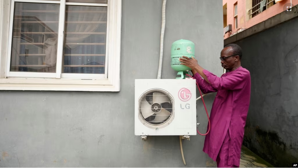 A technician positions an R-22 refrigerant on an outdoor air conditioning unit in Lagos, Nigeria, Thursday, July 18, 2024. (AP Photo/Sunday Alamba)