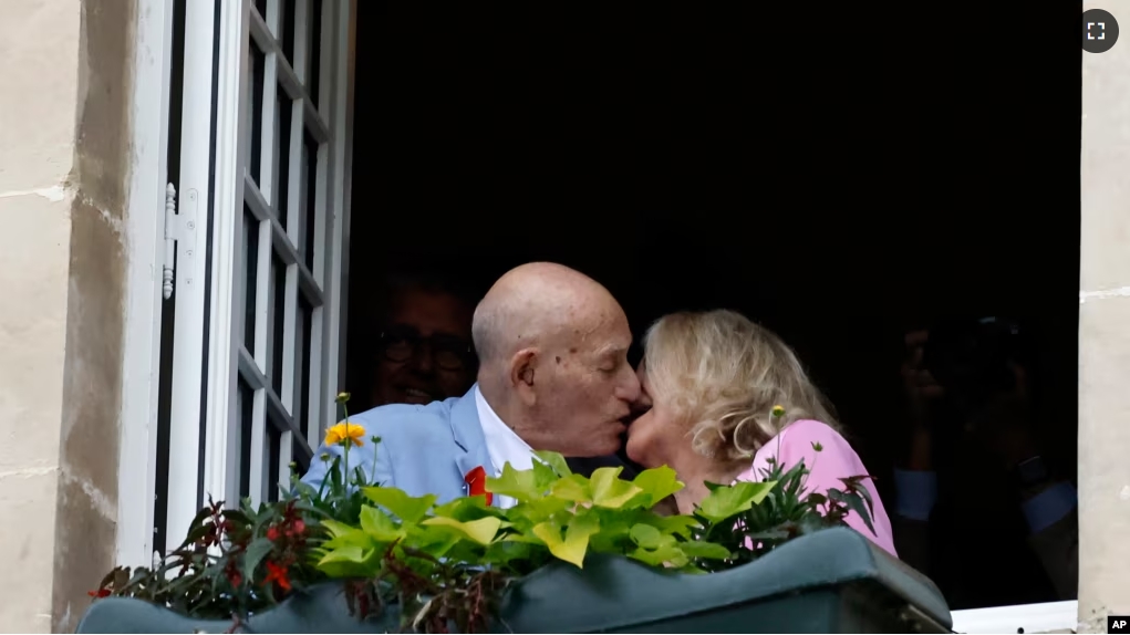 FILE - US WWII veteran Harold Terens, 100, left, and Jeanne Swerlin, 96, kiss from a window after celebrating their wedding at the town hall of Carentan-les-Marais, in Normandy, France, June 8, 2024. (AP Photo/Jeremias Gonzalez)