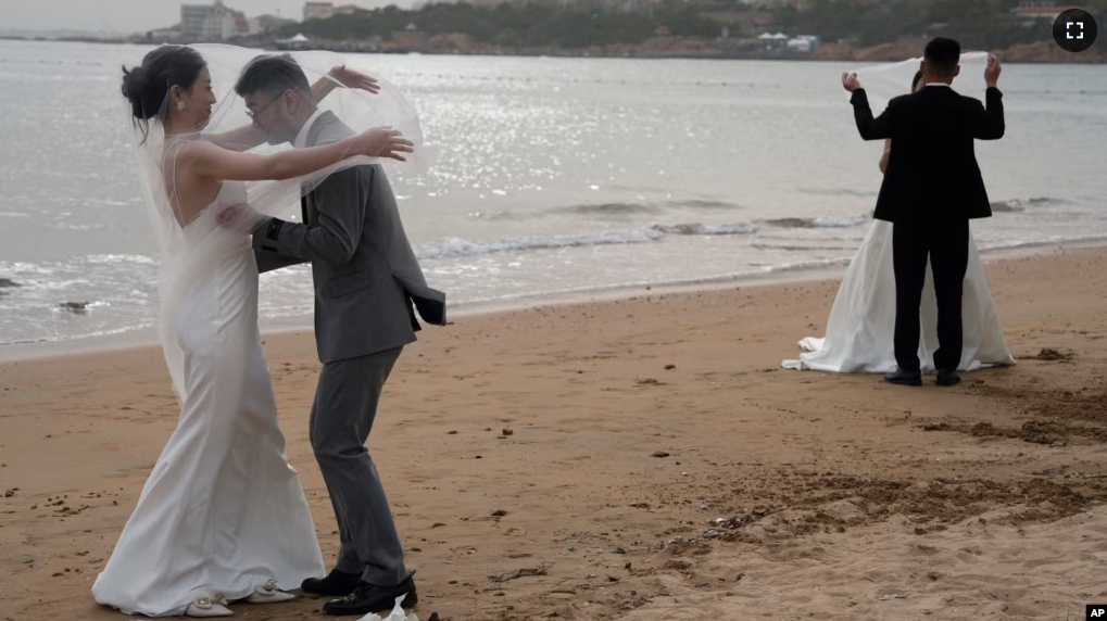 FILE - Wedding couples pose for photos on a beach in Qingdao in eastern China's Shandong province on Friday, April 19, 2024. (AP Photo/Ng Han Guan)