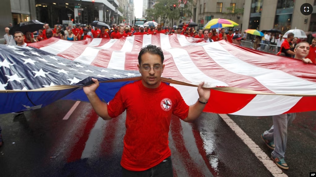 FILE - Iron worker Robert Farula marches up Fifth Ave. carrying an American flag during the Labor Day parade on Sept. 8, 2012, in New York. (AP Photo/Mary Altaffer, File)