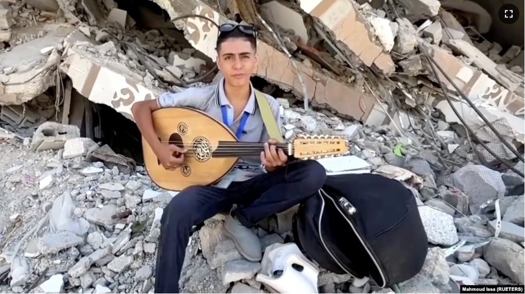 In this frame captured from video, Palestinian teenager Youssef Saad sits on the rubble of his house as he plays oud to bring joy to children, amid Israel-Hamas conflict, in Jabalia refugee camp in the northern Gaza Strip September 2, 2024. (REUTERS/Mahmoud Issa)