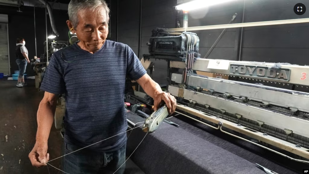 Shigeru Uchida, a weaver at Momotaro Jeans, holds a wooden shuttle next to a vintage loom machine in Kojima, Okayama prefecture, Japan, on Sept. 4, 2024. (AP Photo/Ayaka McGill)