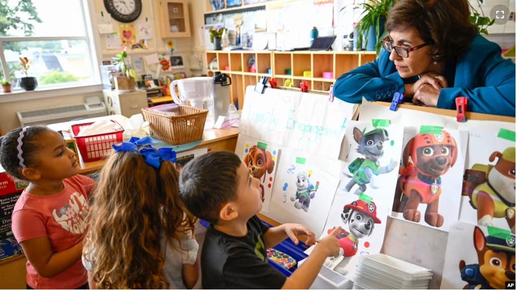 Preschool Executive Director Maria Isabel Ballivian, right, listens to her students on what characters of the TV show PAW Patrol they will vote for at the ACCA Child Development Center on Sept. 19, 2024, in Annandale, Virginia. (AP Photo/John McDonnell)