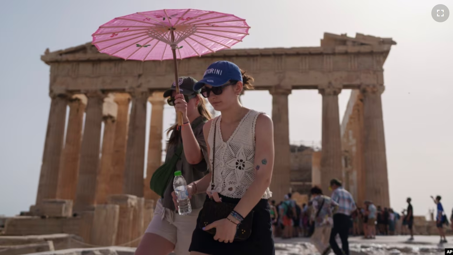 FILE - Tourists with an umbrella walk in front of the Parthenon at the ancient Acropolis in central Athens, June 12, 2024. (AP Photo/Petros Giannakouris, File)