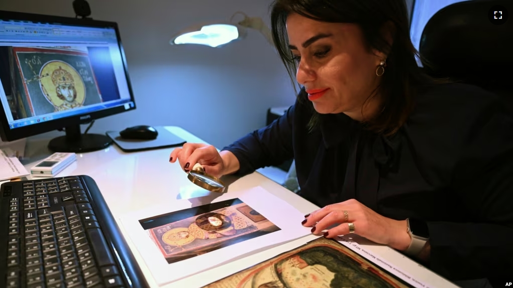 Christina Sotirakoglou a handwriting expert, observes Byzantine paintings based on photographs prints, at her office, in Thessaloniki, northern Greece, Saturday, Nov. 30, 2024. (AP Photo/Giannis Papanikos)