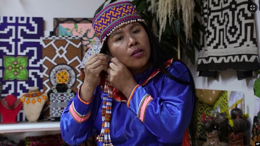 Sadith Silvano, from Paoyhan, a Shipibo-Konibo Indigenous community in the Amazon, puts on an earring at her home and workshop where she hand-paints textiles in Lima, Peru, Saturday, Oct. 19, 2024. (AP Photo/Guadalupe Pardo)