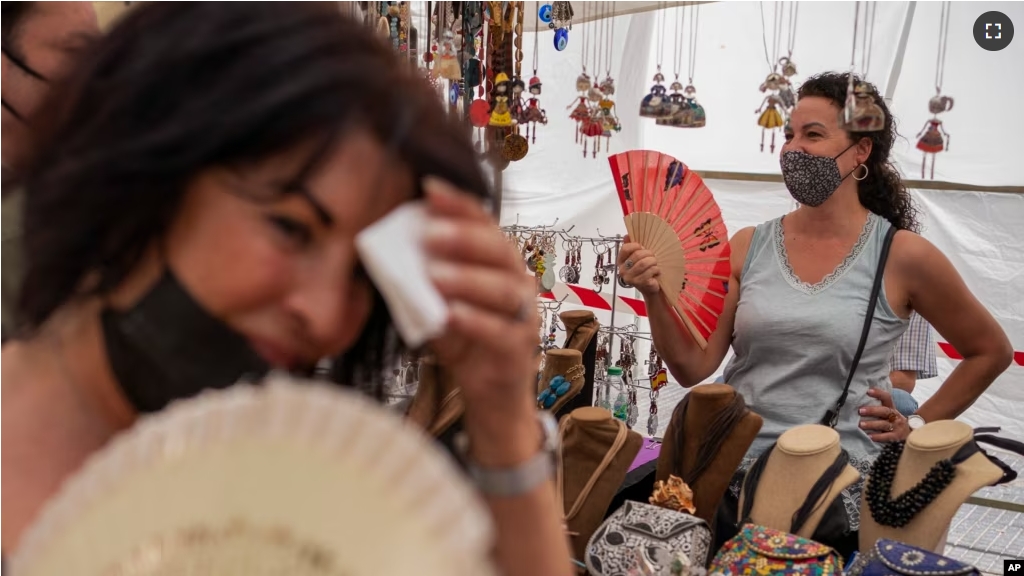 FILE - Women cool themselves with fans in the Rastro flea market during a heatwave in Madrid, Spain, Aug. 15, 2021. (AP Photo/Andrea Comas, file)