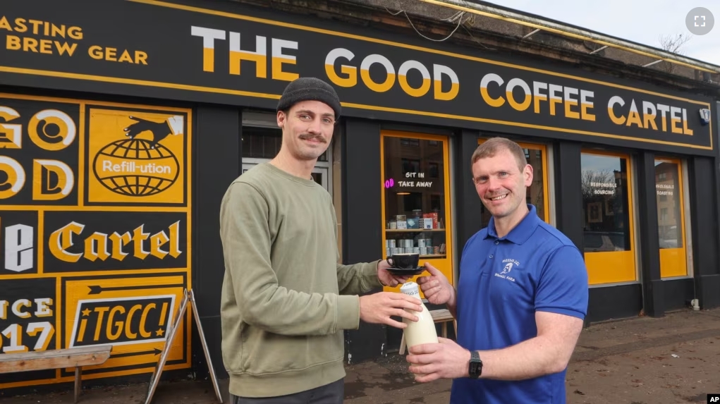 This undated handout photo shows farmer and owner of Mossgiel Organic Farm Bryce Cunningham, right, giving a bottle of milk to barista Jacob Smith, as they pose outside The Good Coffee Cartel in Glasgow, Scotland. (Mossgiel Organic Dairy via AP)