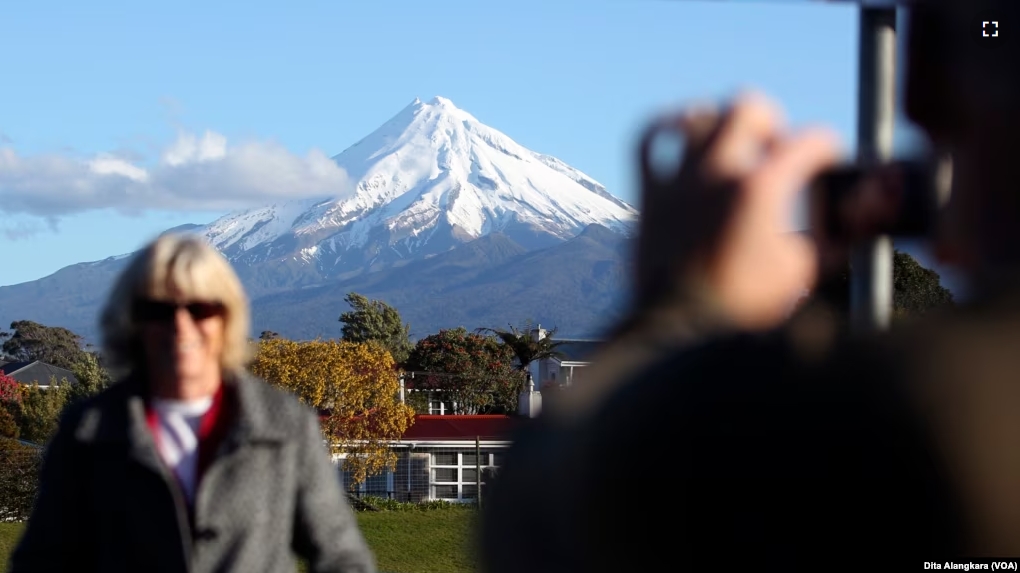 FILE - A man takes a picture of his wife with Mount Taranaki, also known as Mount Egmont, in the background in New Plymouth, New Zealand, Sept. 26, 2011. (AP Photo/Dita Alangkara, File)
