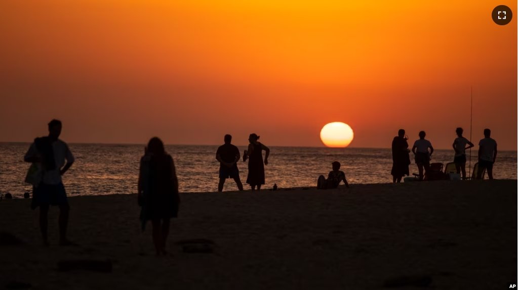 In this file photo, people watch a sunset sitting on a beach next to the Trafalgar Lighthouse in Los Caños de Meca, Spain, on, July 29, 2020. (AP Photo/Emilio Morenatti, File)