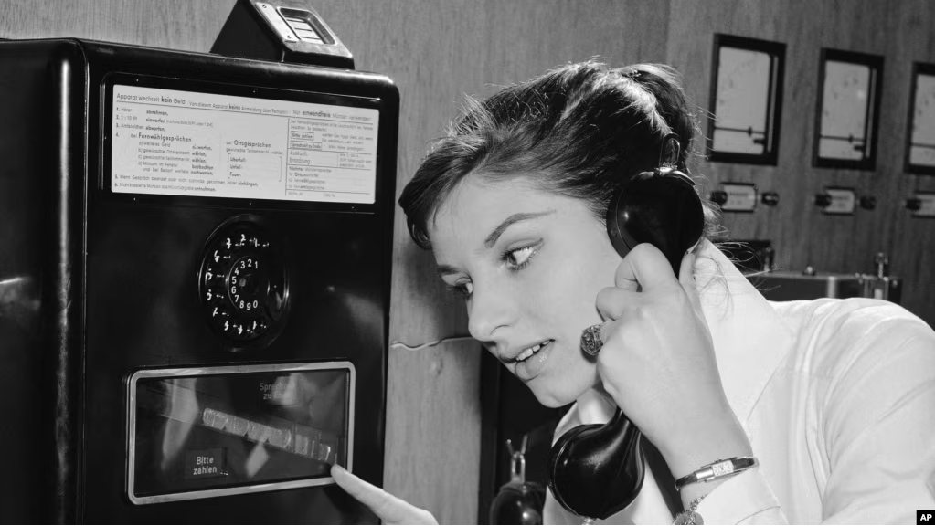 As coins slide down before her eyes, a German woman uses a new long distance dial telephone for public booths, July 17, 1957. (AP Photo)